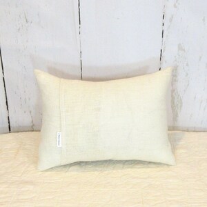 May include: A white rectangular cushion with a subtle texture. The cushion has a seam down the centre and a small white tag with the text "Rustic Collection" on the side.