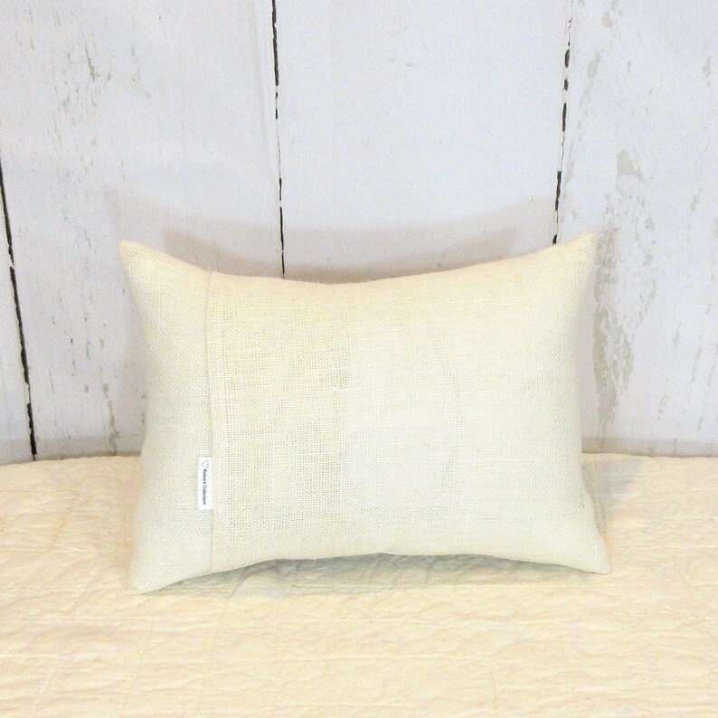 May include: A white rectangular cushion with a subtle texture. The cushion has a seam down the centre and a small white tag with the text "Rustic Collection" on the side.