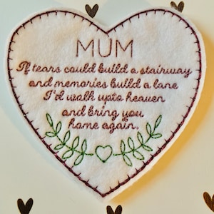 May include: A white felt heart with a pink embroidered border and a green embroidered floral design. The heart has a pink embroidered message that reads "MUM If tears could build a stairway and memories build a lane I'd walk upto heaven and bring you home again."