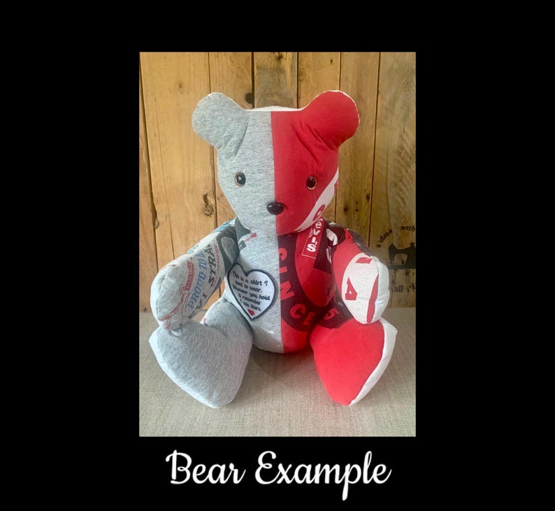 May include: A handmade teddy bear with a split design. One side is gray, the other is red with white text. The bear has a heart-shaped patch with text. The bear is sitting on a light-colored surface.