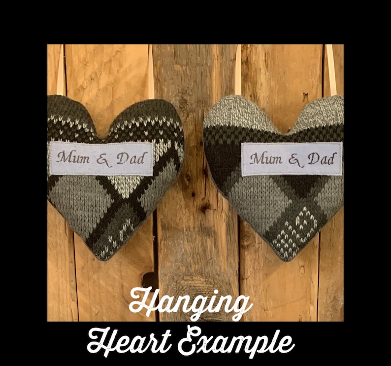 May include: Two heart-shaped fabric ornaments with a gray and green argyle pattern. Each heart has a white label with the embroidered text "Mum & Dad". The hearts hang from a cream-colored ribbon against a wooden background.