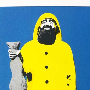 Könnte beinhalten: Grußkarte mit einer Pop-Art-Illustration eines Fischers in einem gelben Regenmantel, der einen großen Fisch hält. Der Hintergrund ist blau und die Karte ist weiß umrandet.