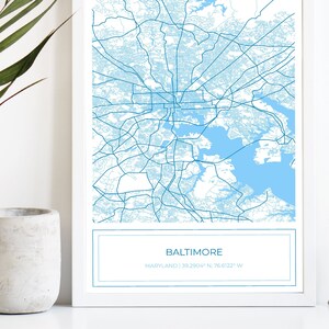 May include: A blue and white map print of Baltimore, Maryland with the city's name and coordinates printed below the map.