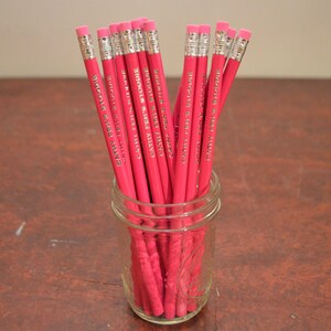 May include: A glass jar filled with pink pencils, each with the text "Cathy Peele Studio" printed on them.