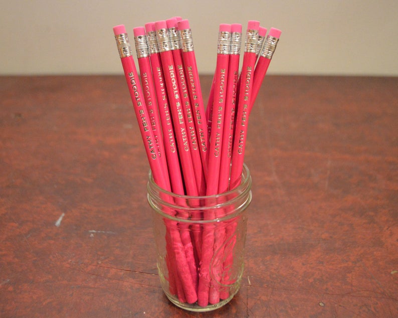 May include: A glass jar filled with pink pencils, each with the text "Cathy Peele Studio" printed on them.