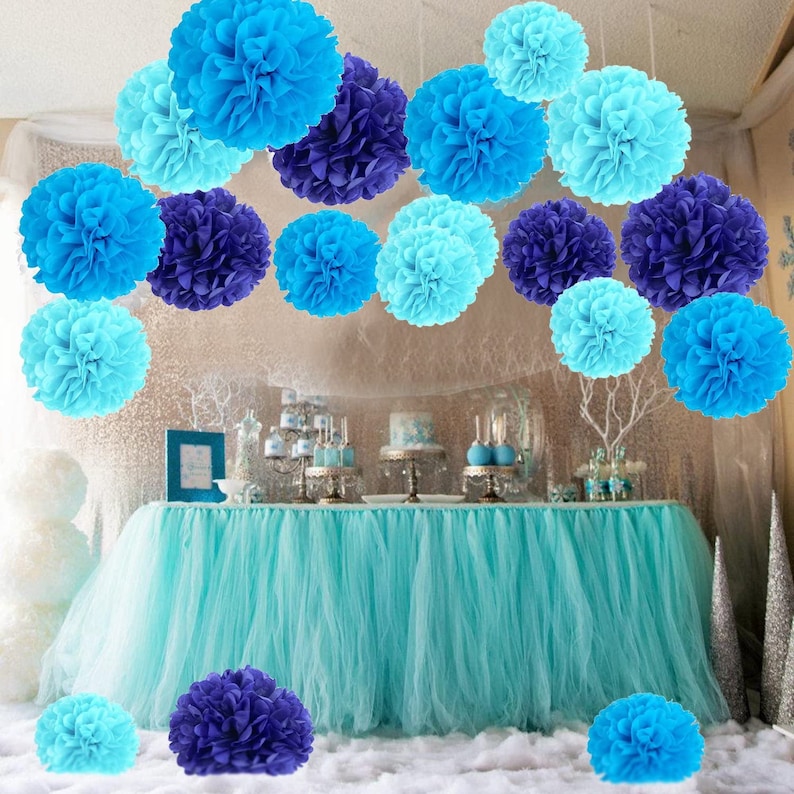 May include: A turquoise table skirt with blue and light blue tissue paper pom-poms hanging above it. The pom-poms are arranged in a row and are a popular party decoration.