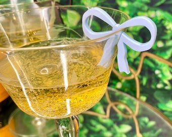 Peut inclure: Une coupe de champagne avec un charme en forme de nœud bleu clair. Le verre est sur un plateau doré avec un fond vert.