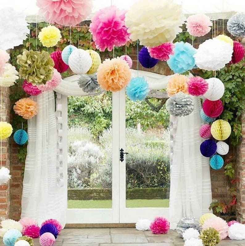 May include: A variety of colorful tissue paper pom-poms and honeycomb balls are hung from the ceiling, creating a festive and whimsical atmosphere. The decorations are arranged in a cascading pattern, with the largest pom-poms at the top and the smaller honeycomb balls at the bottom.