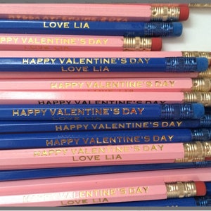 May include: A stack of pink and blue pencils with gold lettering that reads "Happy Valentine's Day" and "Love Lia".