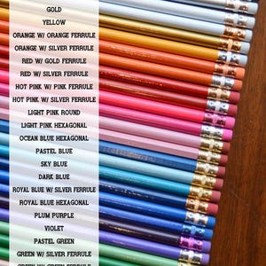 May include: A collection of colored pencils with different colored ferrules. The pencils are arranged in a row from black to natural. The colors include black, silver, white, gold, orange, red, hot pink, light pink, ocean blue, pastel blue, sky blue, dark blue, royal blue, plum purple, violet, pastel green, and green.
