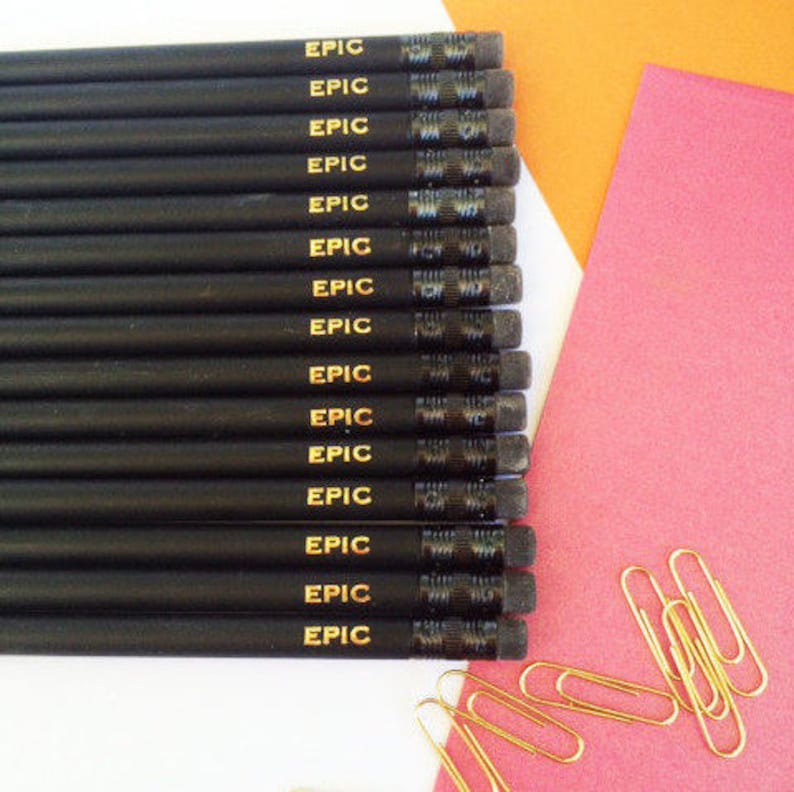 May include: A set of black pencils with gold lettering that says "EPIC" on each pencil. The pencils are arranged vertically and are on a white surface.