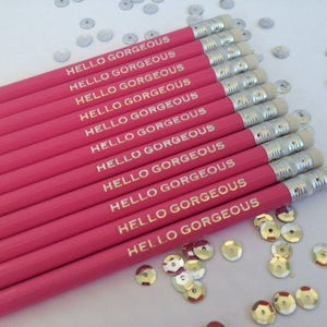 May include: A set of pink pencils with gold lettering that reads "Hello Gorgeous" on each pencil. The pencils are arranged in a stack with the erasers facing up.