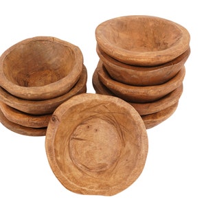 May include: A stack of eight small, wooden bowls, all with a natural brown color and a slightly rough texture. The bowls are stacked in a pyramid shape, with the largest bowl at the bottom and the smallest bowl at the top. One bowl is laying flat on the table.