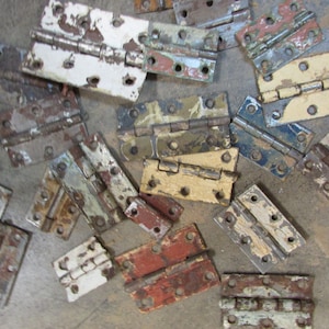 May include: A collection of vintage door hinges with various colors of paint, including white, blue, green, yellow, and brown. The hinges are made of metal and have a rustic look.