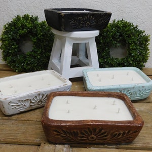 Pu&ograve; includere: Quattro candele rettangolari in contenitori decorativi. I contenitori sono bianchi, marroni, blu chiaro e neri. Le candele sono tutte bianche e hanno pi&ugrave; stoppini.