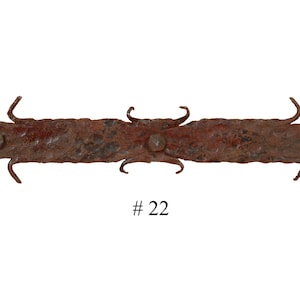 May include: A rusty metal hinge with a pointed end and three prongs on each side. The hinge is marked with the number "#22".