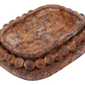 May include: A rustic, rectangular ceramic dish with a textured, mottled brown and orange finish. The dish has a raised, oval-shaped interior and is surrounded by a border of small, round beads. The base is also rectangular.
