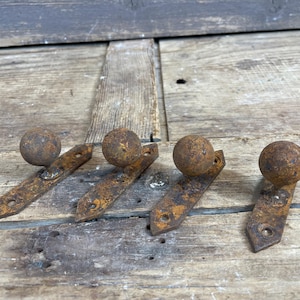 May include: Four rusty metal hooks with round ball finials. The hooks are attached to a wooden surface.