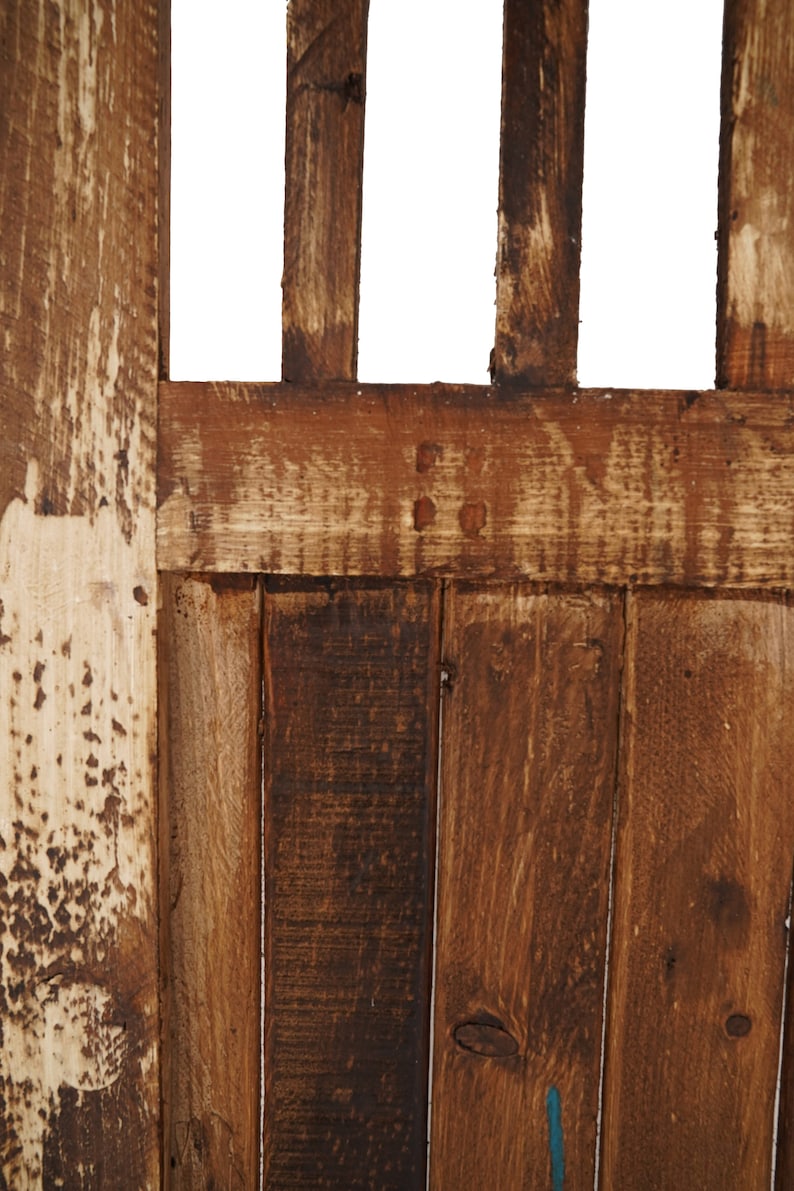 May include: Close-up of a wooden door with a weathered, brown finish. The door is made of vertical planks with a horizontal plank across the top. The wood has a natural grain pattern and shows signs of age and wear.