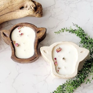 May include: Two wooden candle holders shaped like a cow's head. The candle holders are filled with white candles and dried flowers. One candle holder is brown and the other is white.