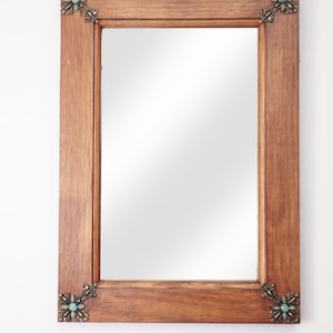 May include: A wooden framed mirror with ornate brass corners featuring turquoise stones. The mirror has a simple, rectangular shape.