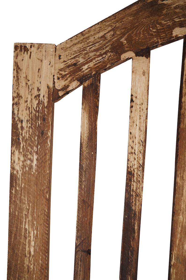 May include: Close-up of a wooden chair back with a distressed brown finish. The chair back has vertical slats and a curved top.