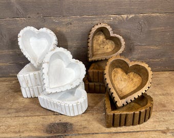 May include: Several heart-shaped wooden bowls, some painted white, others in natural wood tones. The bowls feature carved details and are displayed on a wooden surface, highlighting their decorative and practical use.