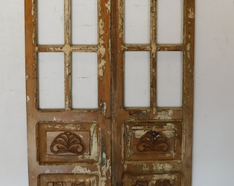 Puede incluir: Un par de puertas de madera antiguas con detalles tallados y múltiples paneles de vidrio. Las puertas están pintadas en un acabado blanco y marrón desgastado.