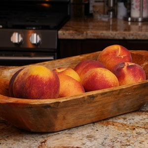 May include: A wooden bowl filled with ripe peaches. The peaches are a mix of red and yellow, and they are arranged in a pleasing pattern. The bowl is made of natural wood and has a rustic look.