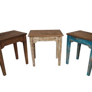 May include: Three small wooden side tables in varying colors. One is dark brown, one is off-white, and the third is blue. Each table has a rectangular top and four angled legs. The tables are likely for decorative use.