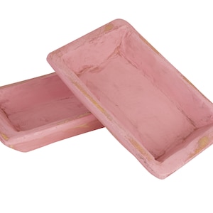 May include: Two pink wooden rectangular trays with a distressed finish. The trays are stacked on top of each other.