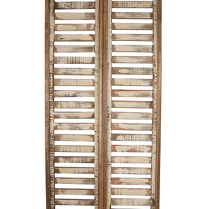 May include: A whitewashed wooden room divider with a rustic, distressed finish. The divider is made of two panels, each with horizontal slats. The panels are hinged together and can be folded for storage.
