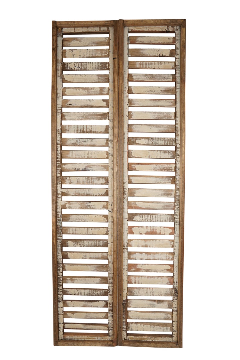 May include: A whitewashed wooden room divider with a rustic, distressed finish. The divider is made of two panels, each with horizontal slats. The panels are hinged together and can be folded for storage.
