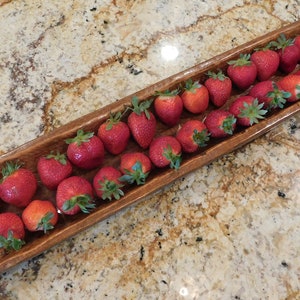 May include: A wooden serving dish filled with fresh, red strawberries. The dish is long and narrow, and the strawberries are arranged in a single row.