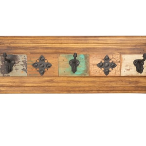 May include: Wooden wall-mounted coat rack with five decorative hooks. The rectangular frame is made of stained wood, with colorful, distressed wooden panels. The hooks are black metal, and the corners are accented with metal studs.