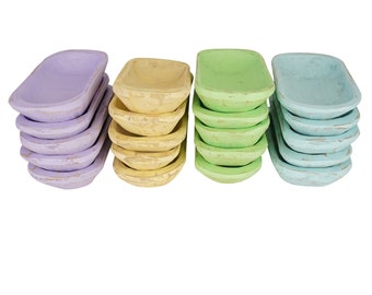May include: A set of four stacks of wooden bowls in pastel colors. The bowls are stacked in a row, with the top bowl of each stack facing the viewer. The bowls are painted in shades of lavender, yellow, green, and blue.