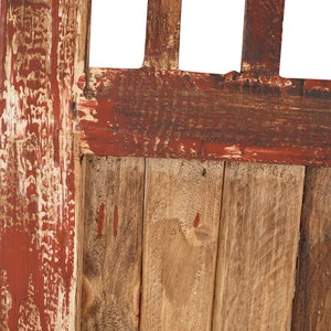 May include: Close-up of a wooden door with red paint that is peeling and chipping. The door is made of vertical planks of wood.