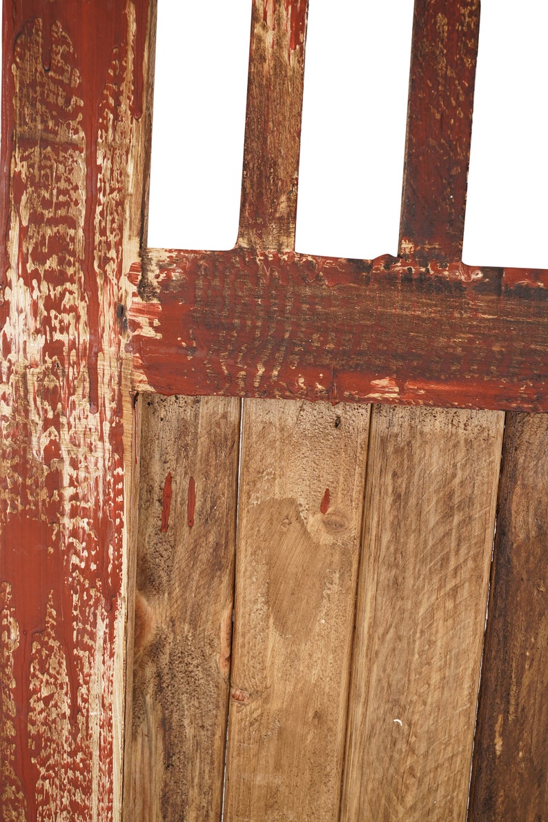 May include: Close-up of a wooden door with red paint that is peeling and chipping. The door is made of vertical planks of wood.