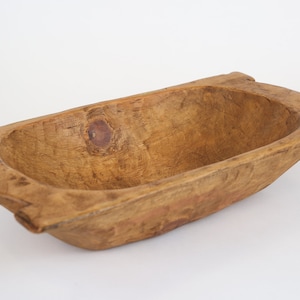May include: A rustic wooden dough bowl with a natural brown finish. The bowl is oval shaped and has a slightly raised rim.