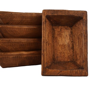 May include: Four brown wooden rectangular serving trays stacked on top of each other. The top tray is standing upright.