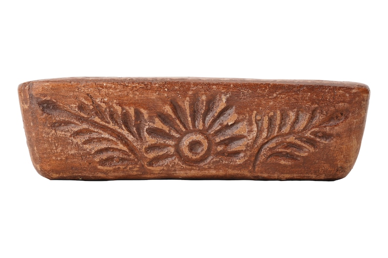 Pu&ograve; includere: Un vaso rettangolare in terracotta marrone con un motivo floreale scolpito. Il vaso ha un fondo leggermente arrotondato e una parte superiore piatta.