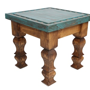 May include: A square wooden end table with a teal blue top and distressed wood finish. The table has four turned legs with a decorative design.