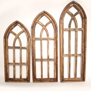 May include: Three wooden arched window frames with a rustic finish. The frames are different sizes and have a decorative grid pattern.
