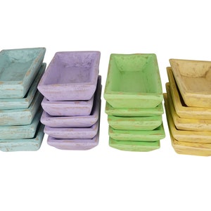 May include: A set of 10 wooden rectangular serving dishes in four colors: light blue, lavender, green, and yellow. The dishes are stacked in four piles of two or three.