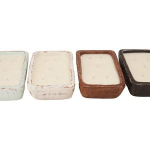 Pu&ograve; includere: Quattro candele rettangolari in contenitori di ceramica di diversi colori. Le candele sono bianche e hanno un aspetto rustico. I contenitori sono blu chiaro, bianco, marrone e nero.