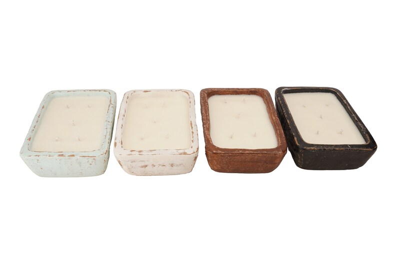 Pu&ograve; includere: Quattro candele rettangolari in contenitori di ceramica di diversi colori. Le candele sono bianche e hanno un aspetto rustico. I contenitori sono blu chiaro, bianco, marrone e nero.