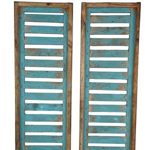 May include: Two wooden shutters painted in a light blue color. The shutters are made of thin wooden slats and have a rustic, weathered look.