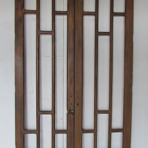 May include: A pair of antique wooden doors with a grid-like design. The doors are made of weathered brown wood and feature rectangular and square openings, creating a window-like appearance. The doors are set against a white background.
