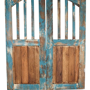 May include: A pair of weathered wooden doors with a blue paint finish. The doors have a decorative arched top and a slatted design. The paint is chipped and faded, giving the doors a rustic look.