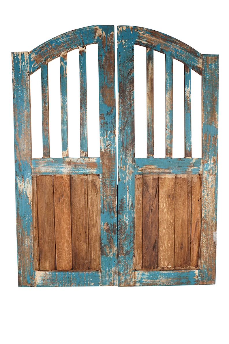 May include: A pair of weathered wooden doors with a blue paint finish. The doors have a decorative arched top and a slatted design. The paint is chipped and faded, giving the doors a rustic look.